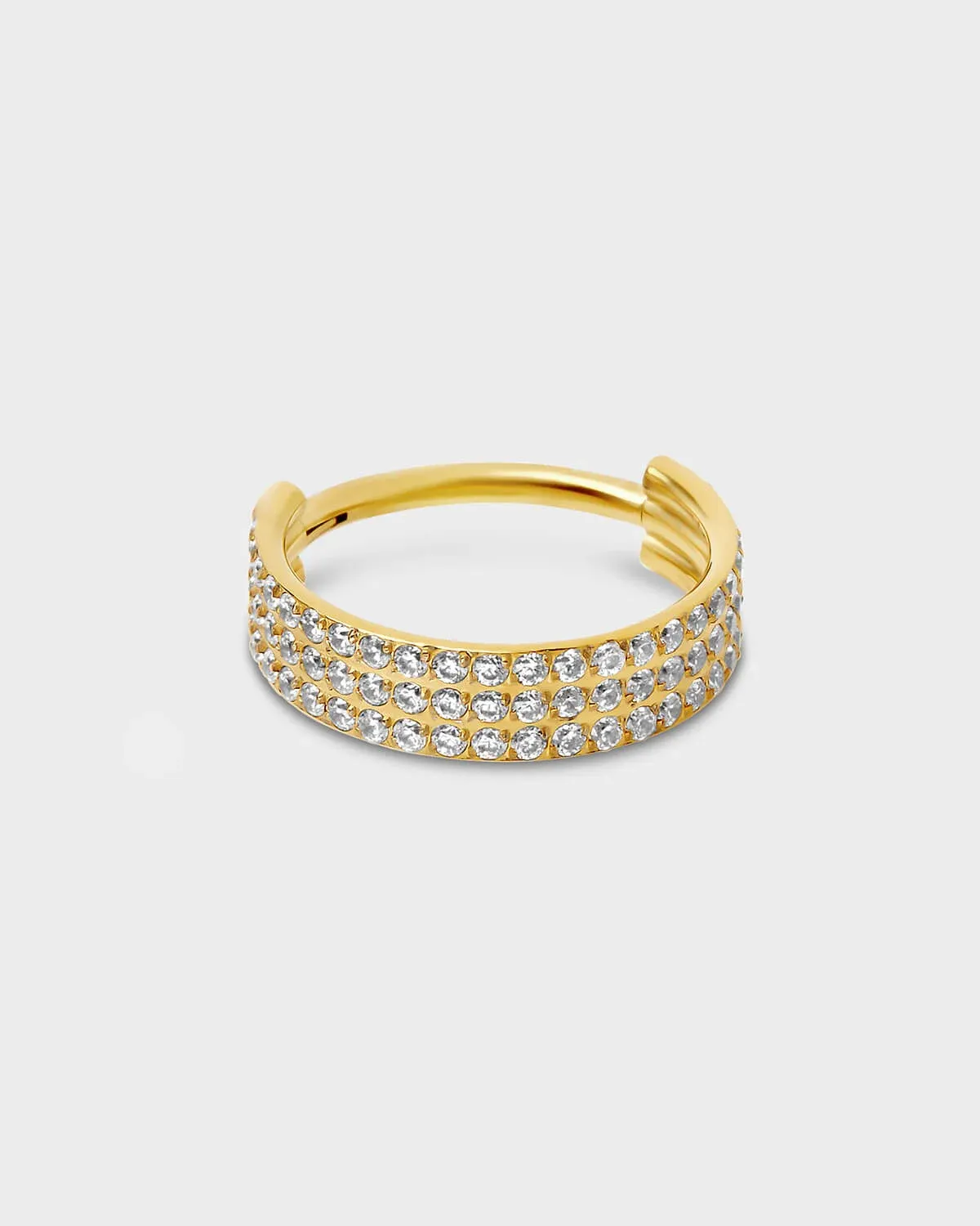 Gold titanium triple and hinged licker ring with pave clear gemstones sat on a light gray background.