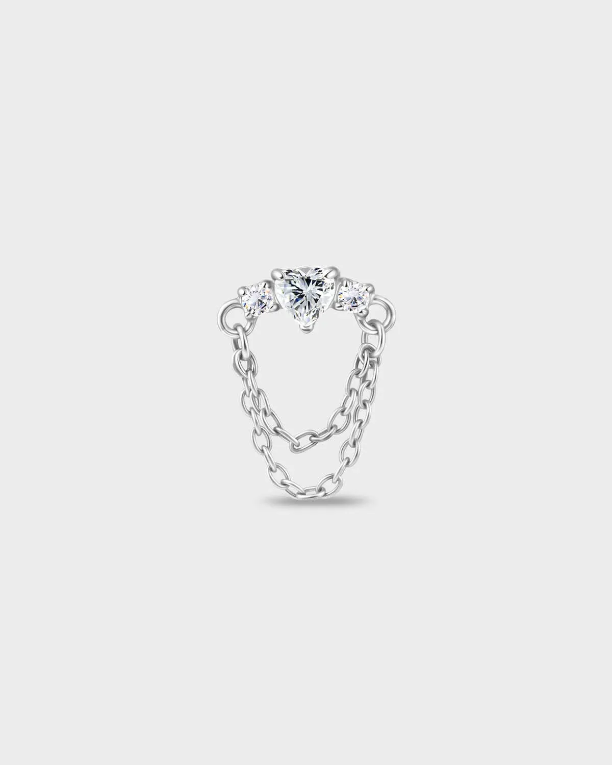 Polished titanium earring with a heart-cut clear stone set between two smaller round-cut stones, finished with a double chain detail on a light gray background.