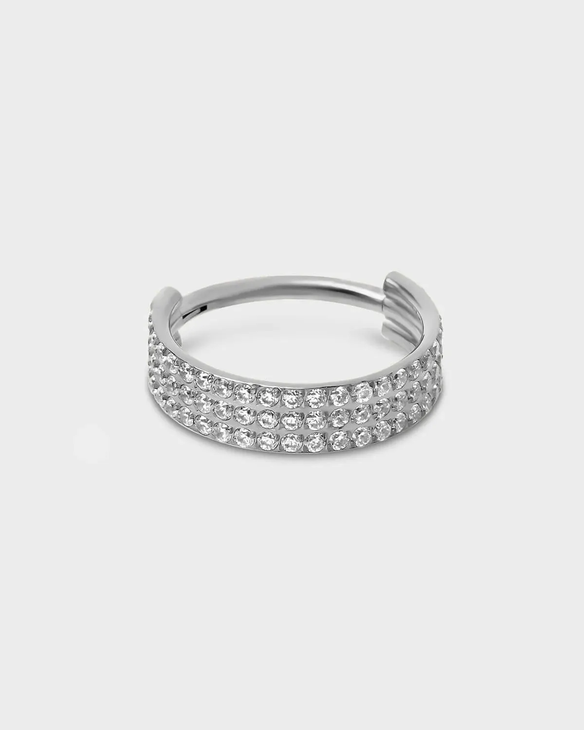 Polished silver titanium triple and hinged licker ring with pave clear gemstones sat on a light gray background.