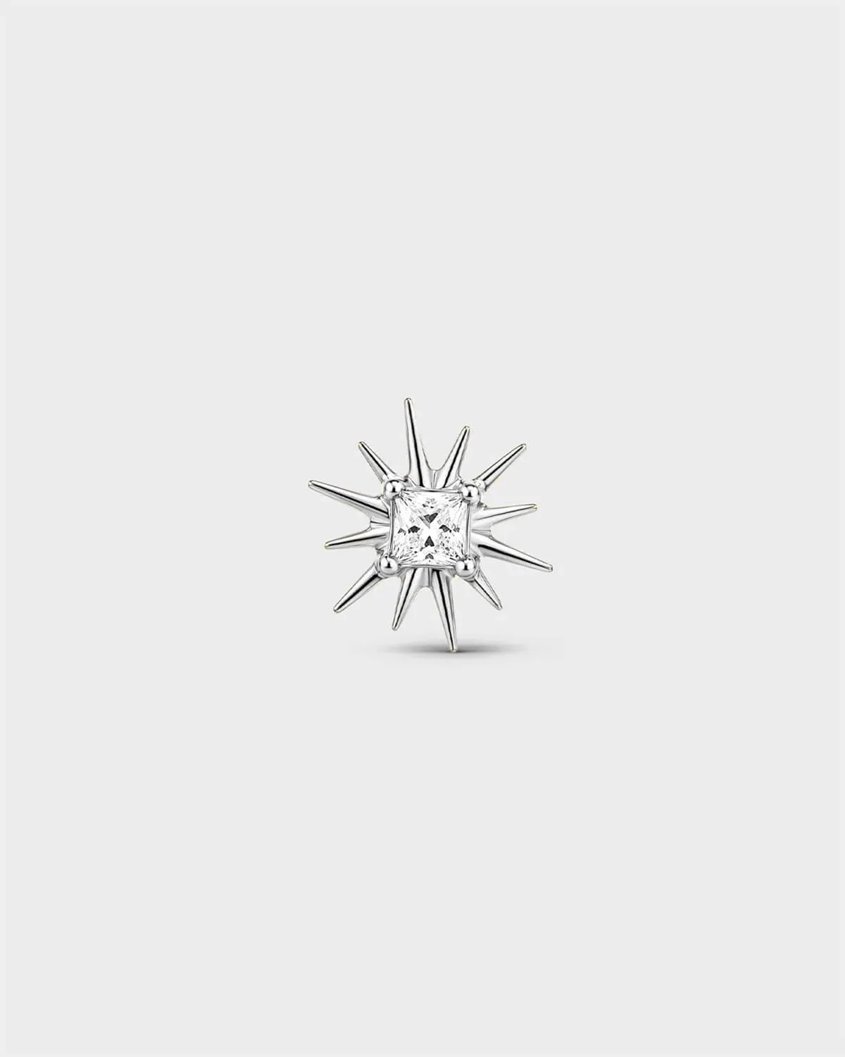 Polished silver titanium threadless end with a princess-cut clear stone set within a sculpted starburst design. On a light grey background.