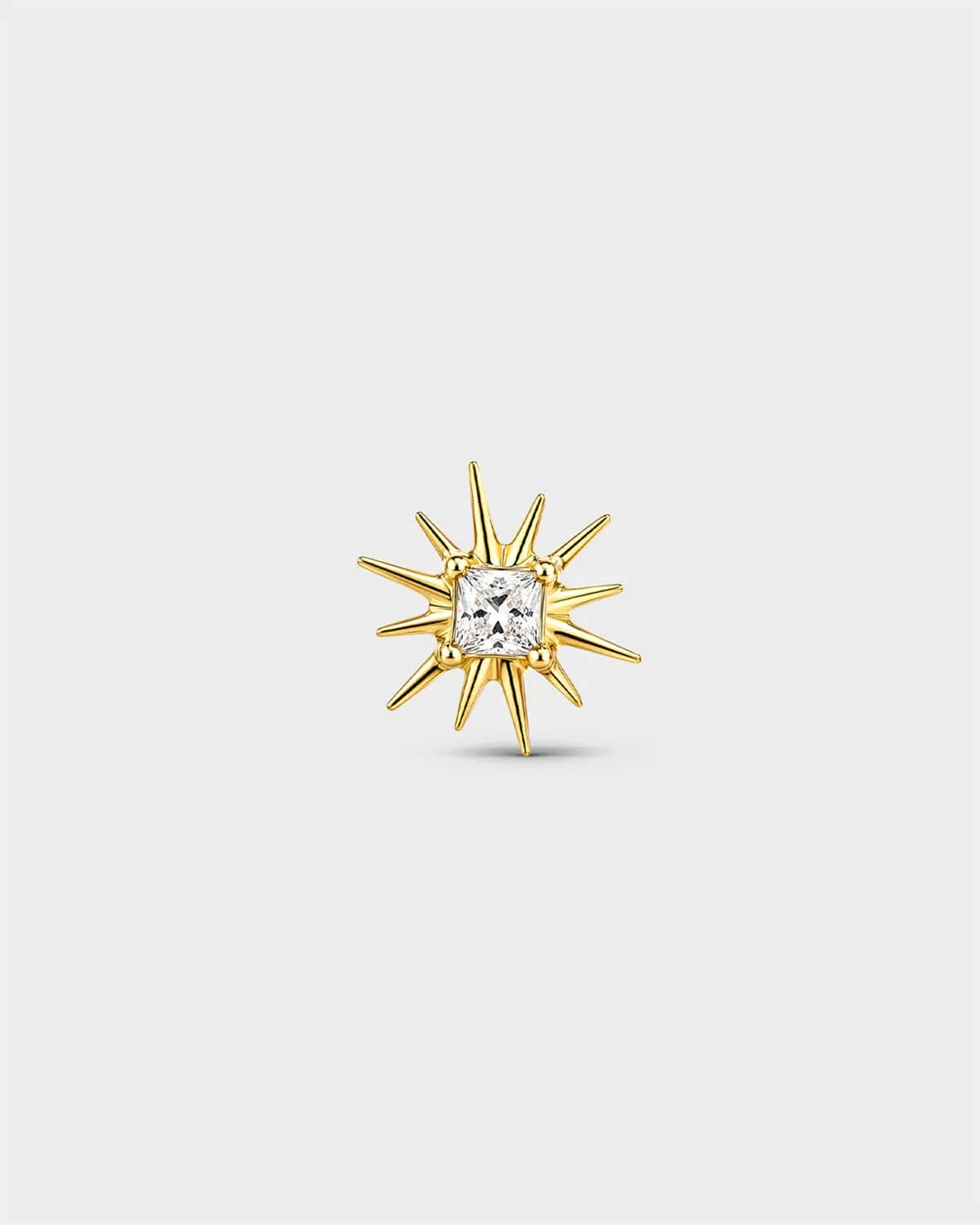 Gold titanium threadless end with a princess-cut clear stone set within a sculpted starburst design. On a light grey background.