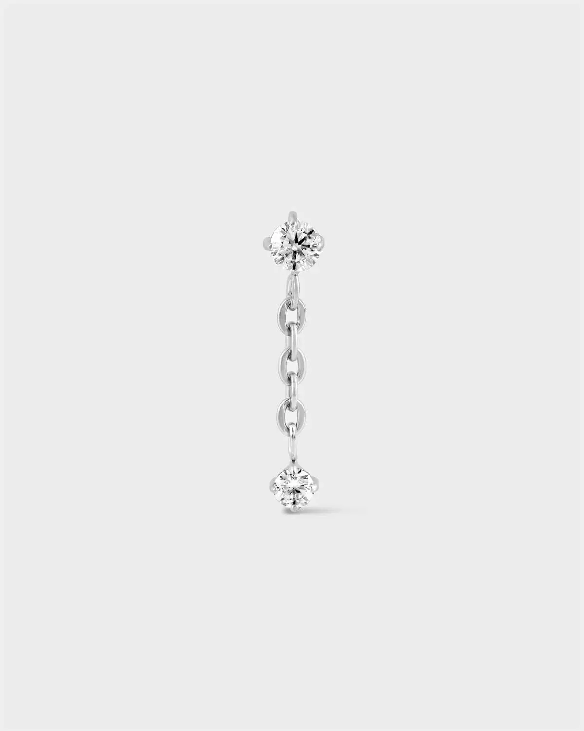 Polished titanium earring with solitaire and chain dropping to another smaller solitaire on a light grey background.
