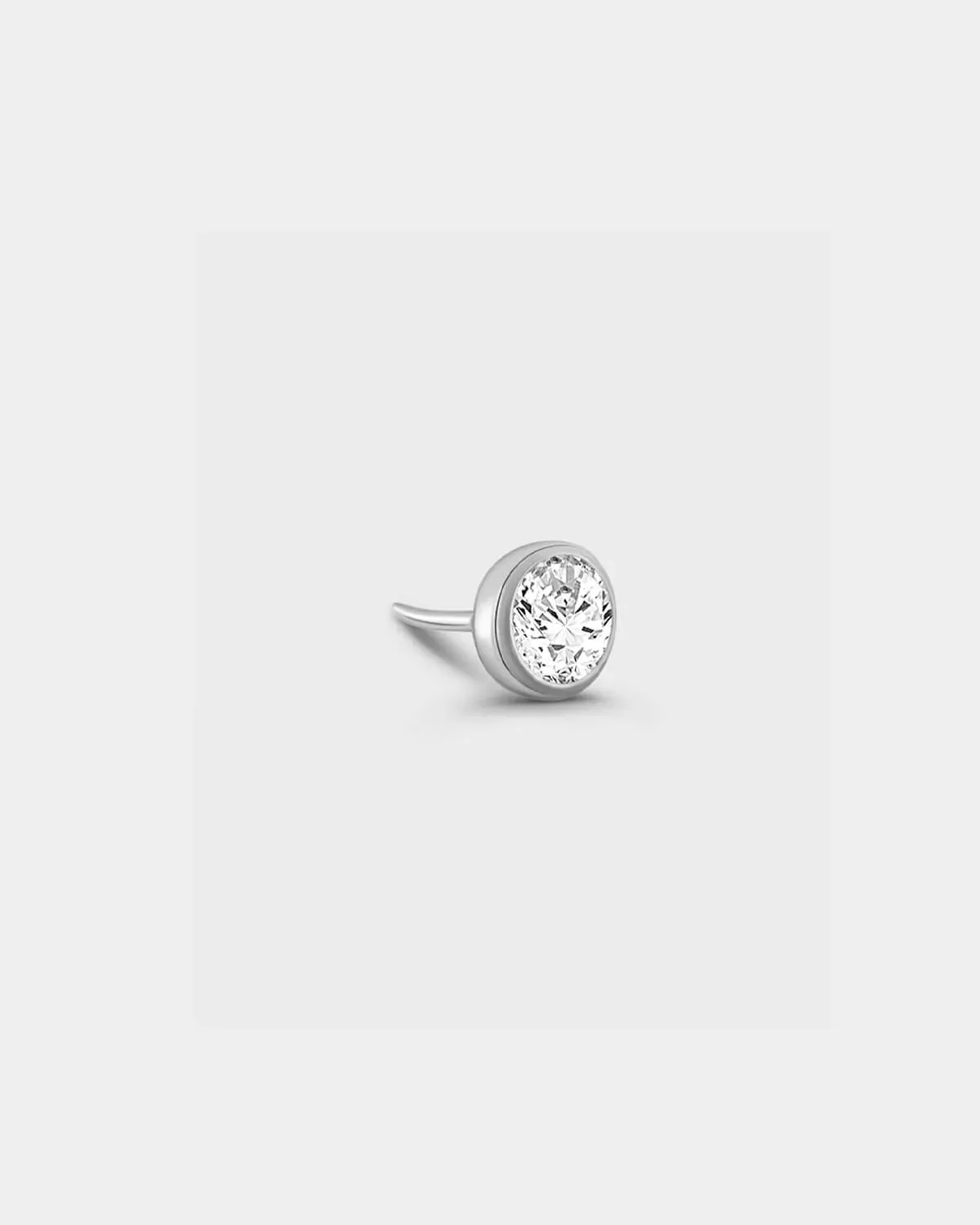 Polished silver titanium bezel set solitaire with clear gemstone n a light grey background.
