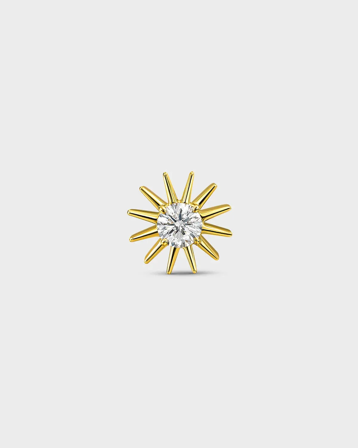 Gold titanium threadless end earring with a round-cut clear stone set within a sculpted starburst design. On a light grey background.