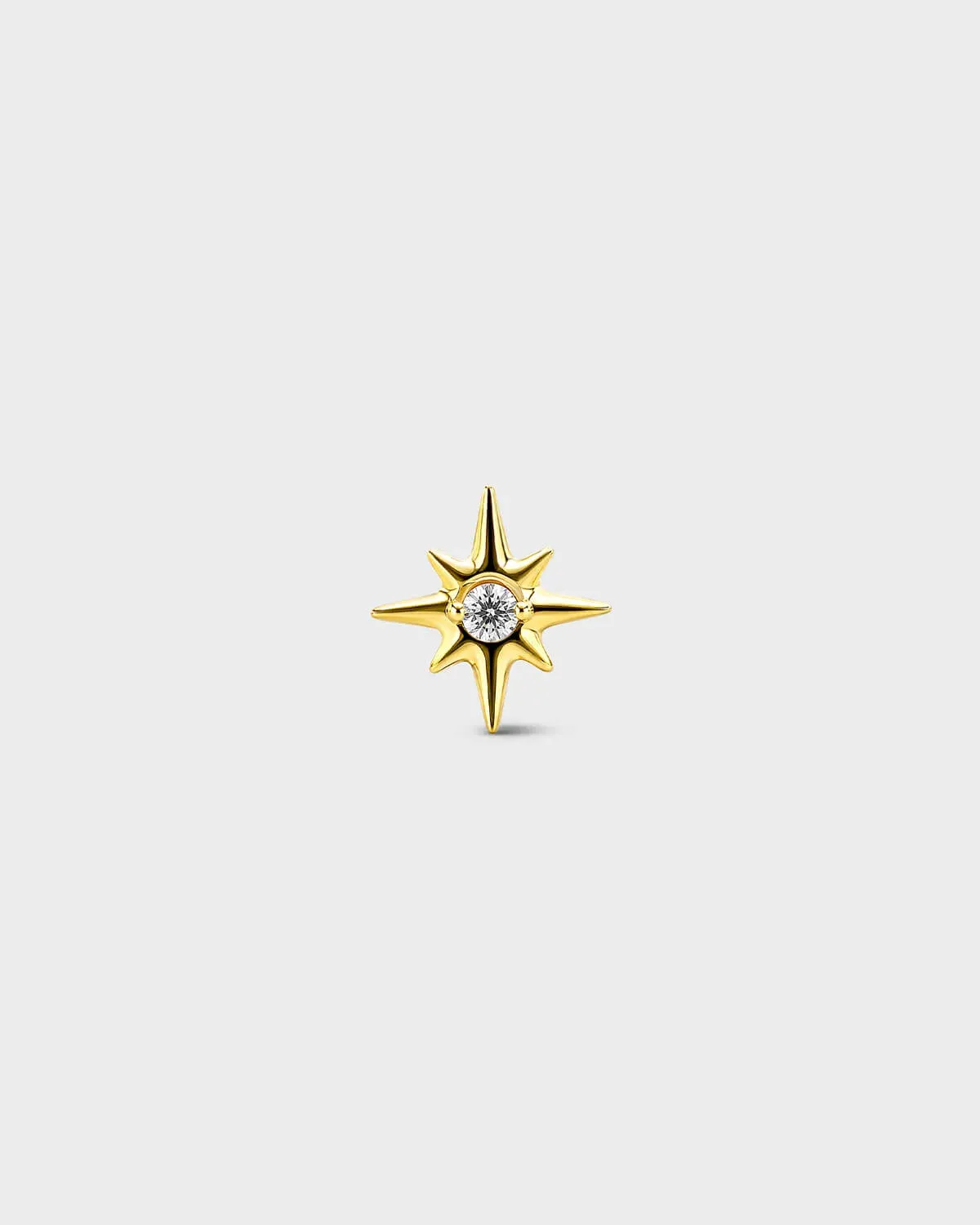 Gold titanium threadless end earring with a round-cut clear stone set within a sculpted star design. On a light grey background.
