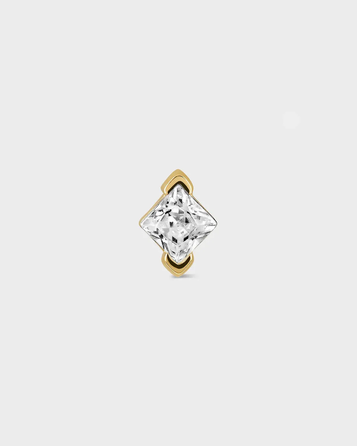 Gold earring with a clear gemstone on a light gray background