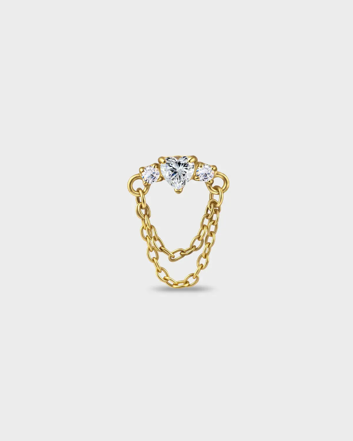 Gold titanium earring with a heart-cut clear stone set between two smaller round-cut stones, finished with a double chain detail on a light gray background.