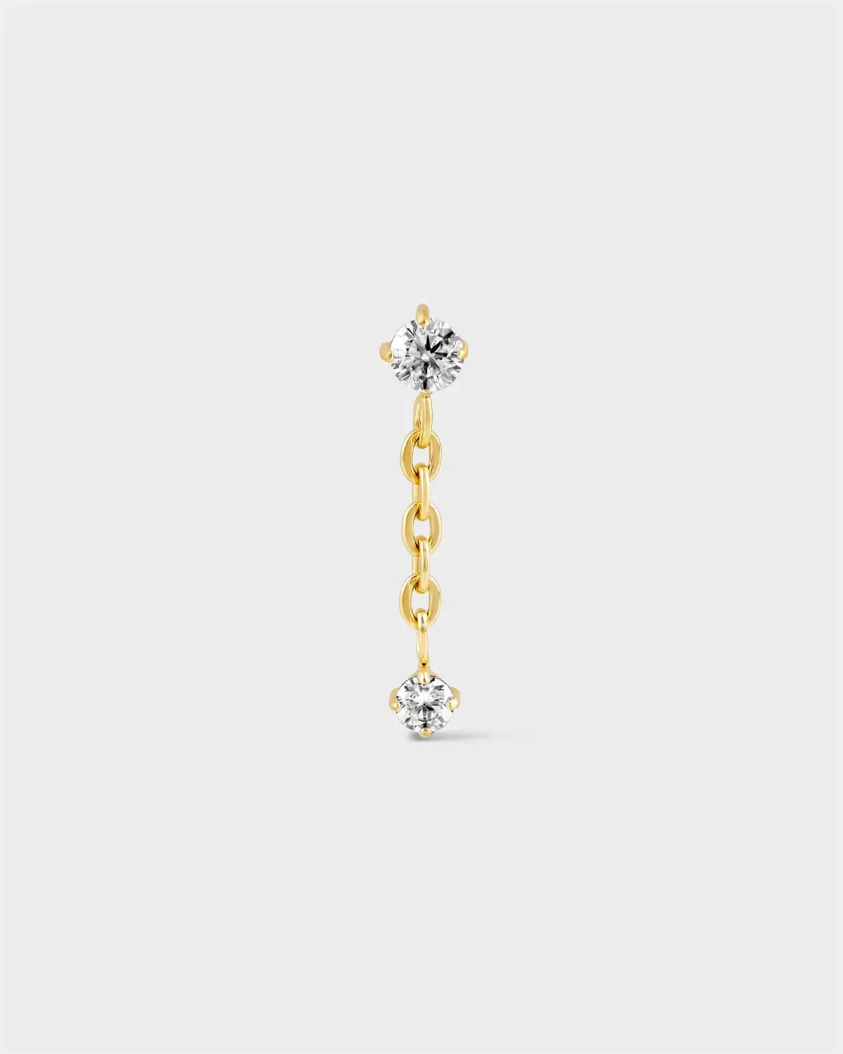Gold titanium earring with solitaire and chain dropping to another smaller solitaire on a light grey background.