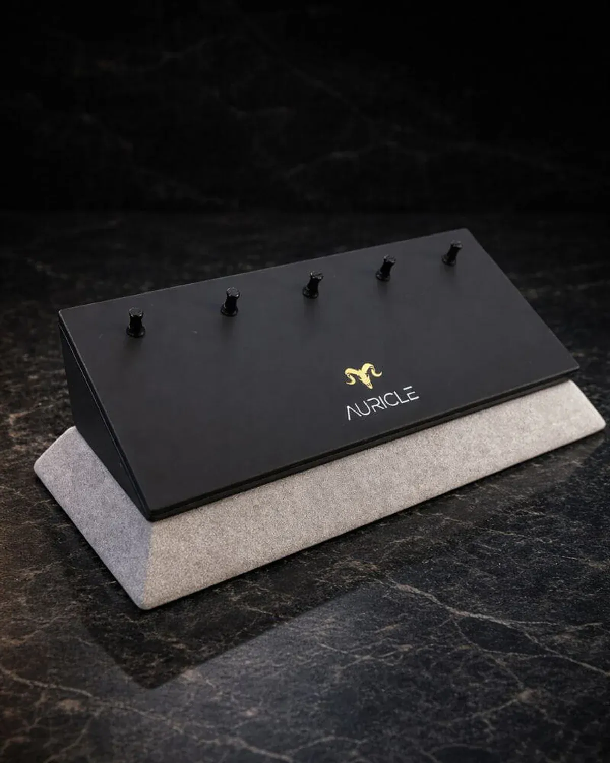jewellery display stand to hold 5 rings. The stand has a light gray suede base with a black leather top. Sat on a dark worktop with moody lighting.