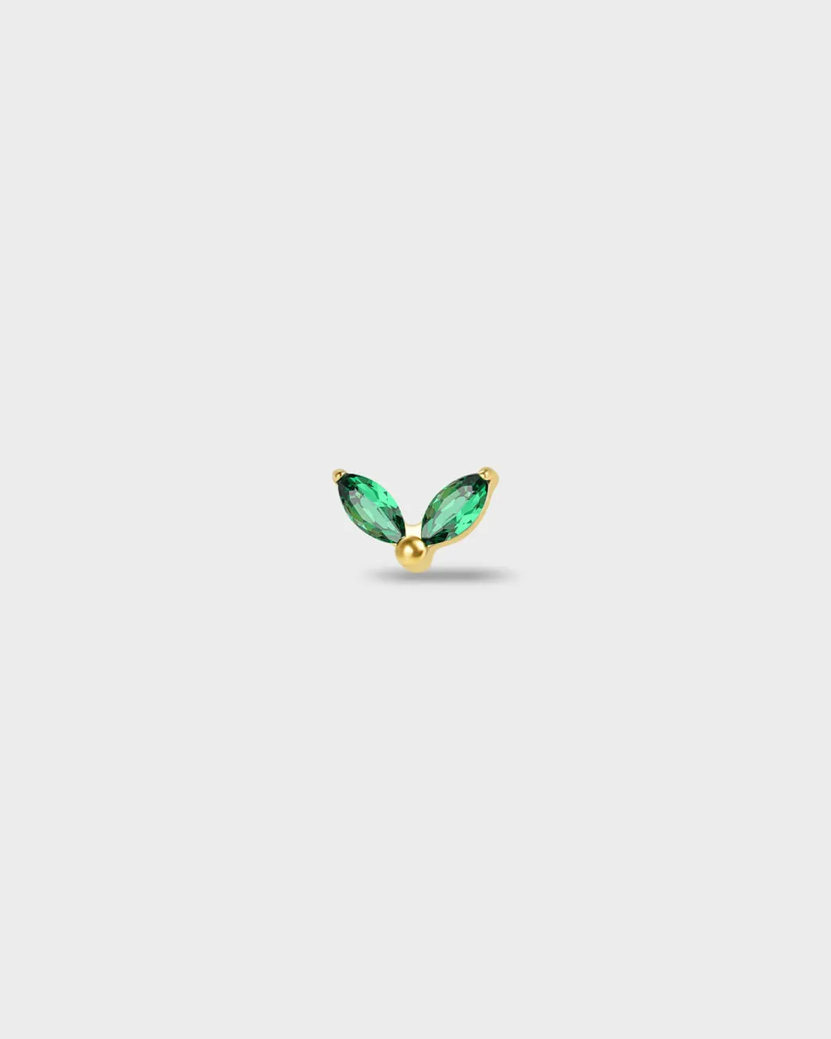 Gold titanium earring with two marquise-cut emerald green stones set in a simple leaf-style arrangement, on a light rgray background.