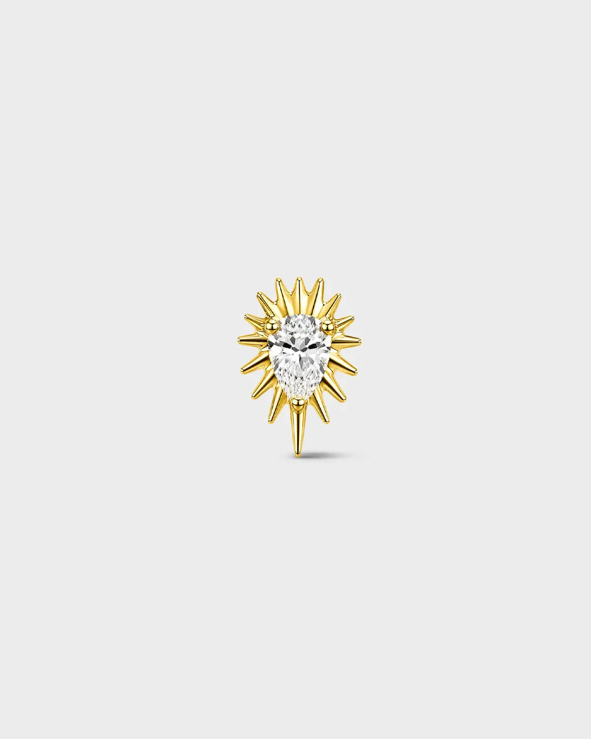 Gold titanium threadless end earring with a pear-cut clear stone set within a sculpted starburst design. On a light grey background.