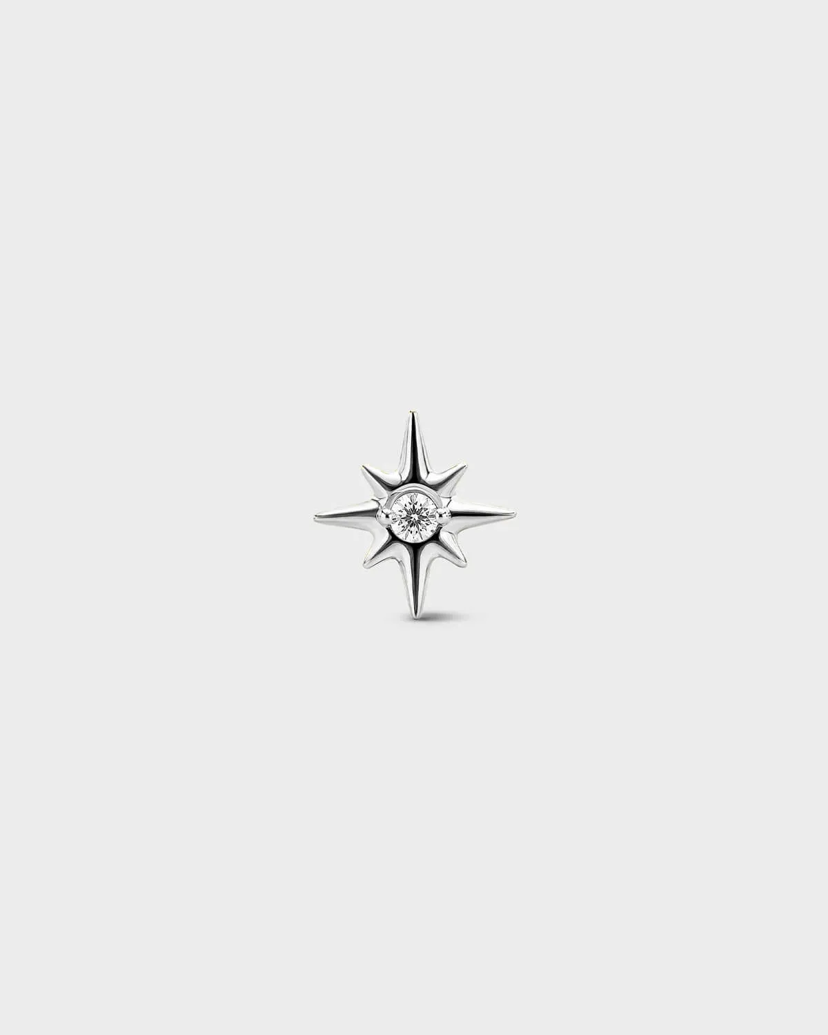 Gold titanium threadless end earring with a round-cut clear stone set within a sculpted star design. On a light grey background.