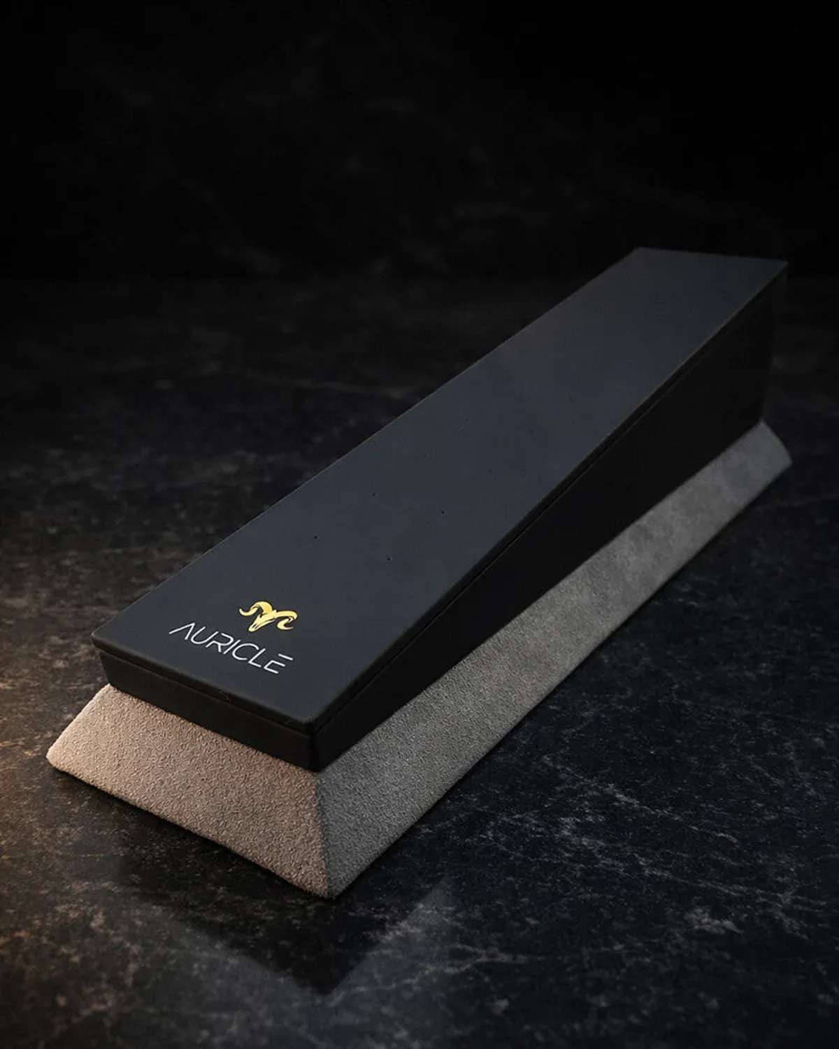 jewellery display stand to hold 20 pieces of jewellery. The stand has a light gray suede base with a black leather top. Sat on a dark worktop with moody lighting.