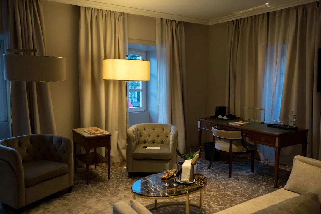 A well-lit hotel room with seating and a desk.