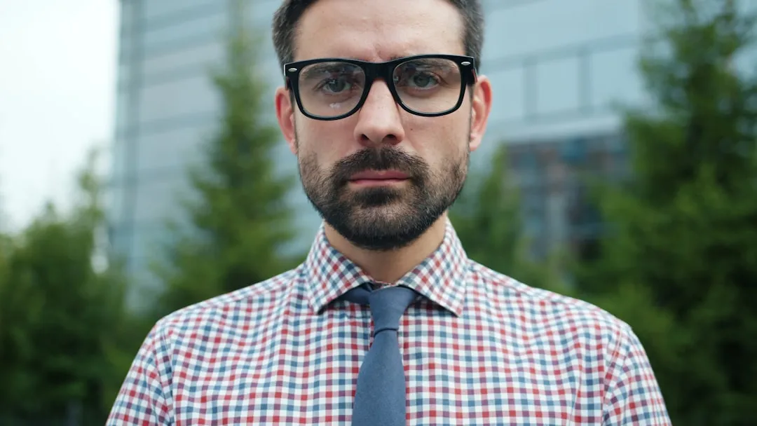 Man with glasses and tie looking directly forward.